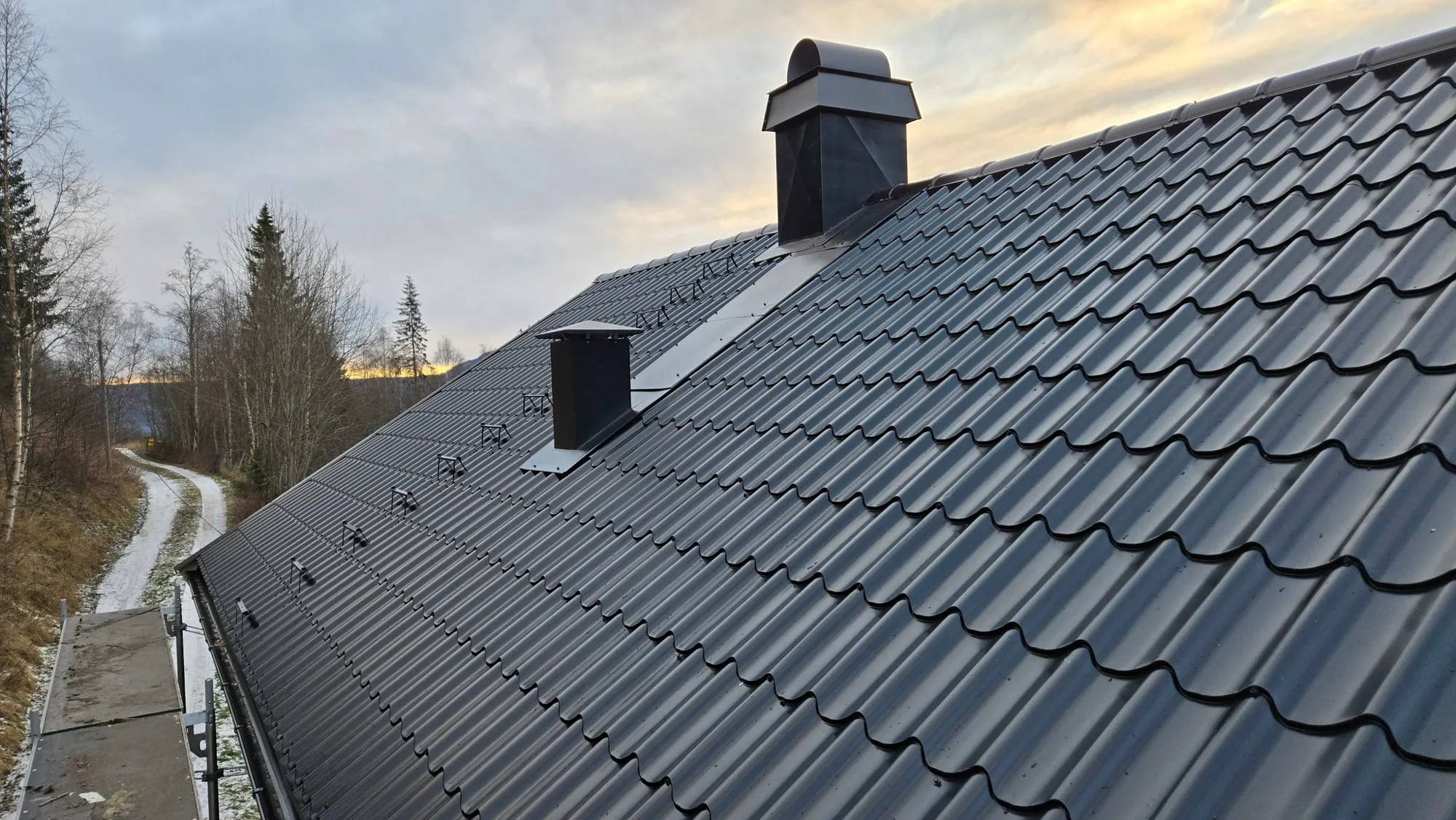Nylagt svart tak med pipebeslag, pipehatt og snøfangere, sett fra stillaset ved takfoten